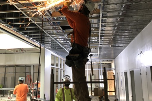 A carpenter standing on scaffolding uses an angle grinder